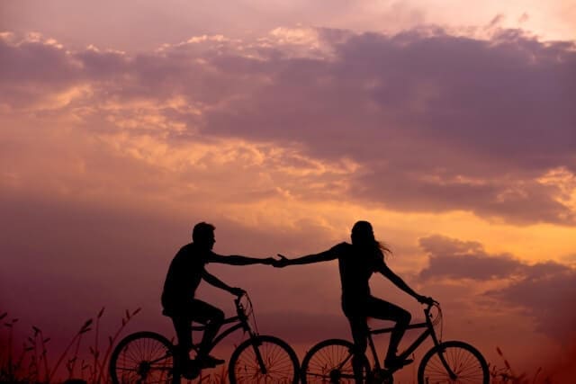 couple on bikes in front of a sunset sky grasping hands